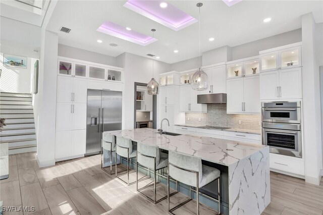 kitchen featuring white cabinetry, hanging light fixtures, a large island, stainless steel appliances, and light stone counters