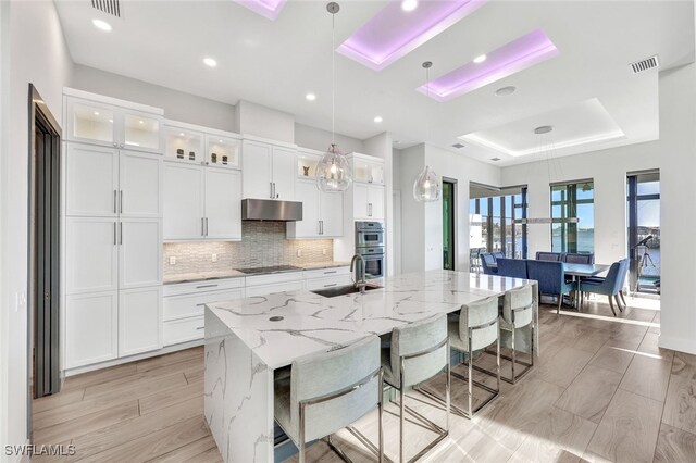 kitchen with decorative light fixtures, white cabinetry, and a kitchen island with sink