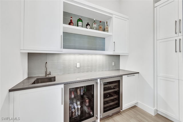 bar featuring sink, white cabinets, stone countertops, and beverage cooler