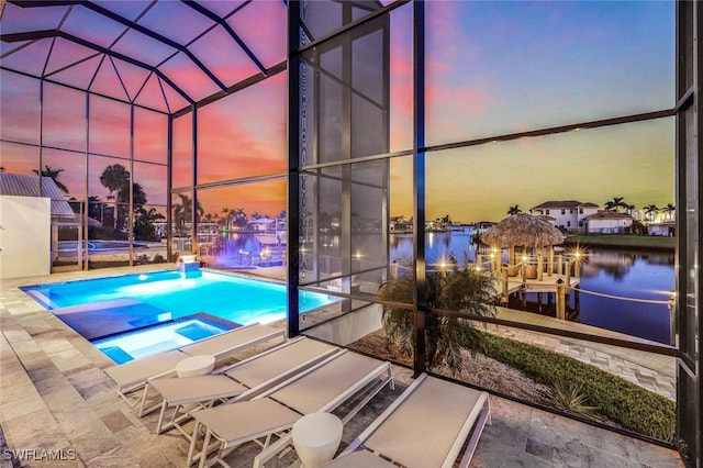 pool at dusk featuring an in ground hot tub, a lanai, a water view, and a patio area