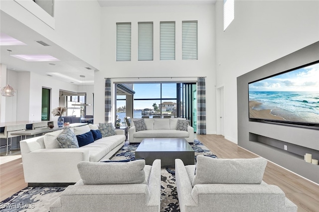 living room featuring plenty of natural light, a towering ceiling, and light wood-type flooring