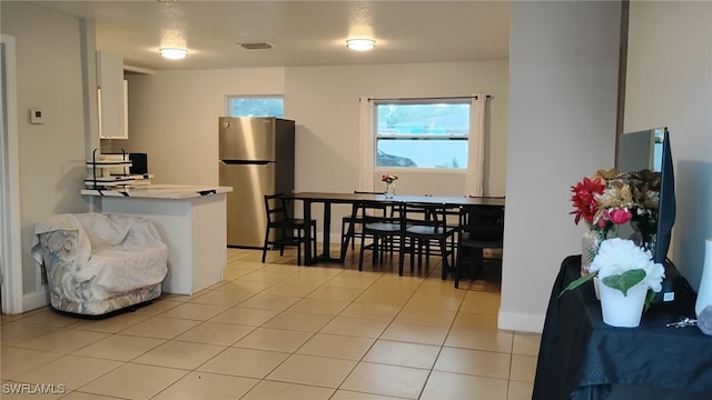 kitchen featuring light tile patterned floors, stainless steel fridge, and white cabinets