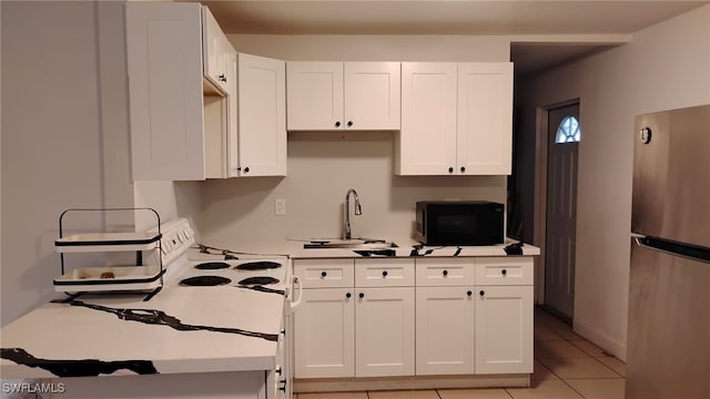 kitchen featuring light tile patterned floors, stainless steel fridge, sink, and white cabinets