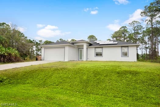 single story home with a garage, solar panels, and a front lawn