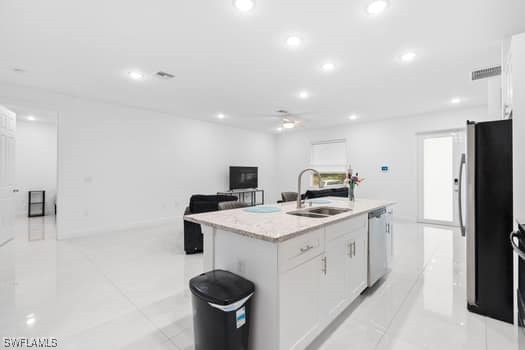 kitchen with appliances with stainless steel finishes, sink, white cabinets, light tile patterned floors, and a center island with sink