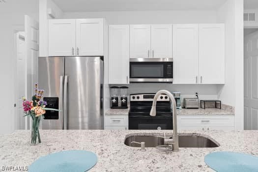 kitchen with sink, white cabinetry, light stone countertops, and stainless steel appliances