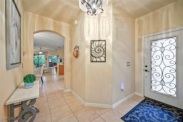 entrance foyer featuring light tile patterned floors, baseboards, arched walkways, and ceiling fan with notable chandelier