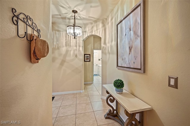 hall with an inviting chandelier, light tile patterned flooring, baseboards, and arched walkways