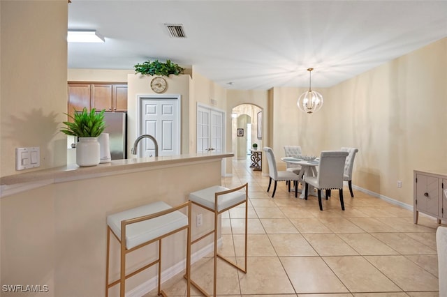 kitchen with freestanding refrigerator, arched walkways, an inviting chandelier, a peninsula, and light tile patterned floors