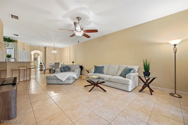 living room featuring light tile patterned floors, visible vents, arched walkways, and ceiling fan