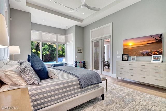 bedroom featuring light hardwood / wood-style flooring, access to outside, ceiling fan, and a tray ceiling