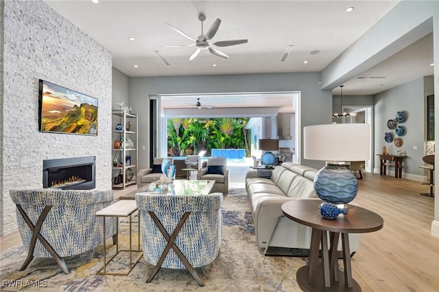 living room with ceiling fan, a stone fireplace, light hardwood / wood-style floors, and built in shelves