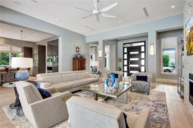 living room with a stone fireplace, a wealth of natural light, ceiling fan, and light hardwood / wood-style flooring