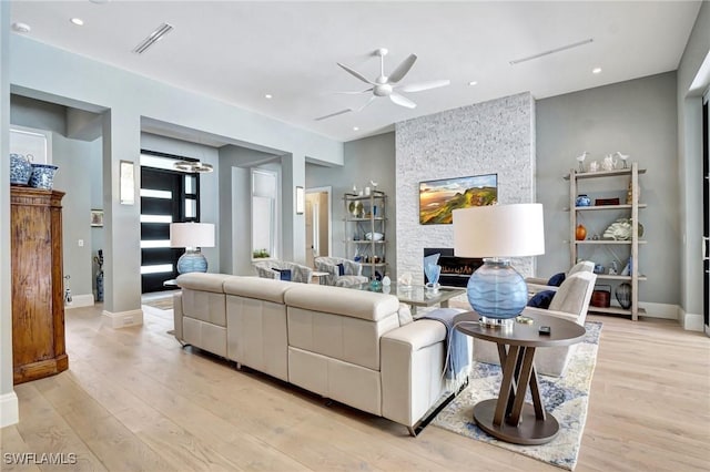 living room featuring ceiling fan, a stone fireplace, and light wood-type flooring