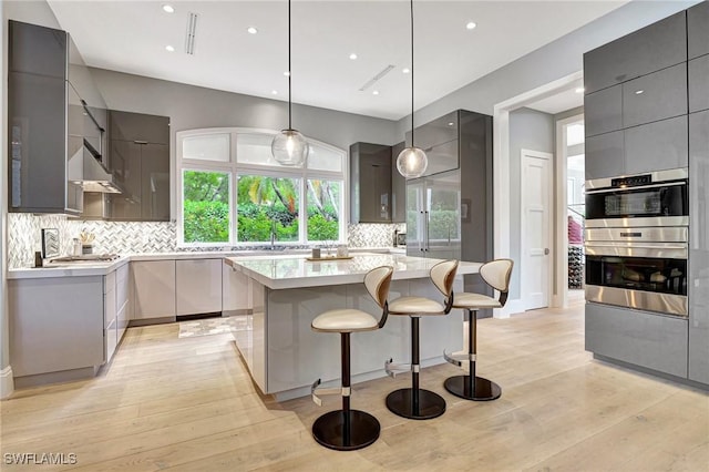 kitchen with decorative backsplash, decorative light fixtures, a kitchen island, and gray cabinetry