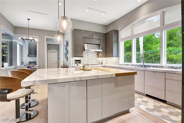 kitchen featuring extractor fan, a kitchen island, decorative light fixtures, sink, and gray cabinetry