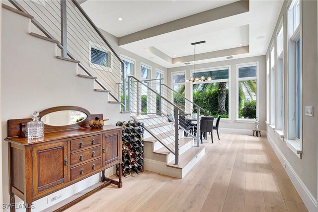 stairway featuring a raised ceiling, hardwood / wood-style floors, and an inviting chandelier