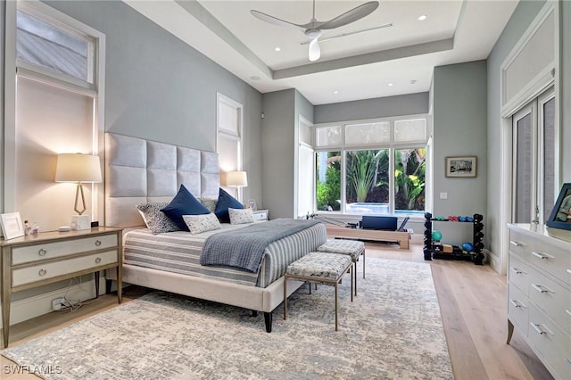 bedroom with ceiling fan, light hardwood / wood-style floors, and a tray ceiling