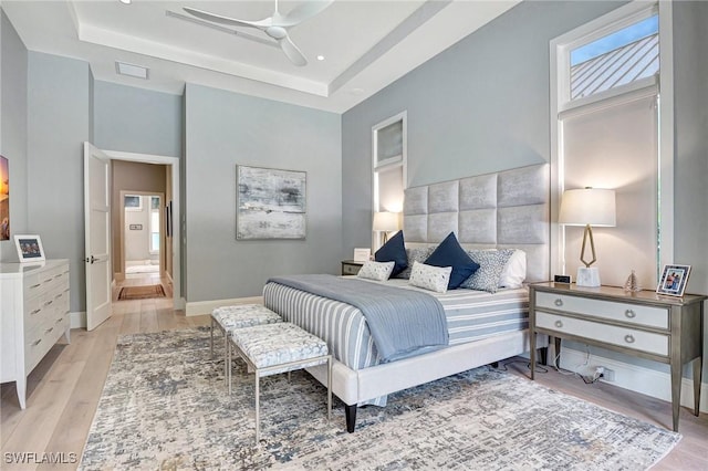 bedroom with a raised ceiling, ensuite bathroom, ceiling fan, and light hardwood / wood-style flooring