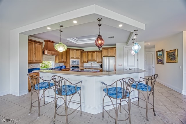 kitchen with a breakfast bar area, premium range hood, stainless steel appliances, a spacious island, and decorative light fixtures