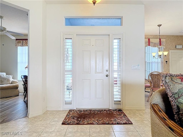 entrance foyer featuring a healthy amount of sunlight, ceiling fan with notable chandelier, and light tile patterned floors