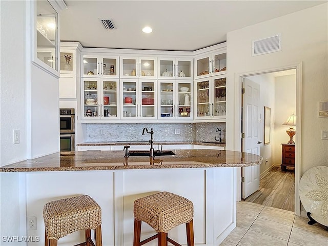 kitchen with tasteful backsplash, white cabinetry, sink, a kitchen bar, and dark stone counters