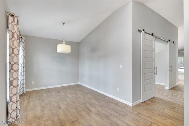 spare room featuring lofted ceiling, a barn door, and light wood-type flooring