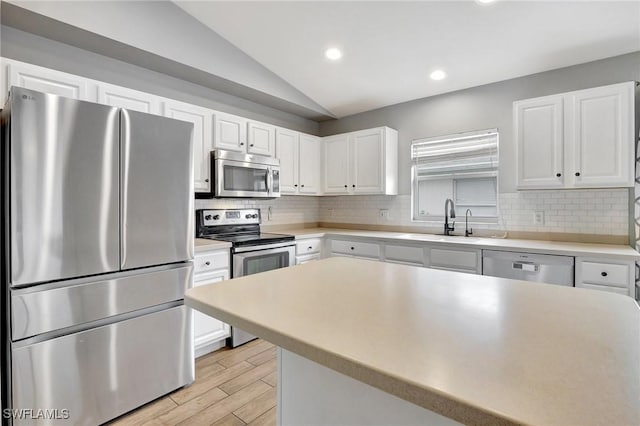 kitchen with vaulted ceiling, sink, white cabinets, light hardwood / wood-style floors, and stainless steel appliances