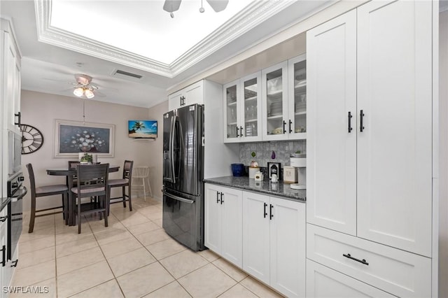 kitchen featuring light tile patterned floors, ceiling fan, black refrigerator, white cabinets, and dark stone counters