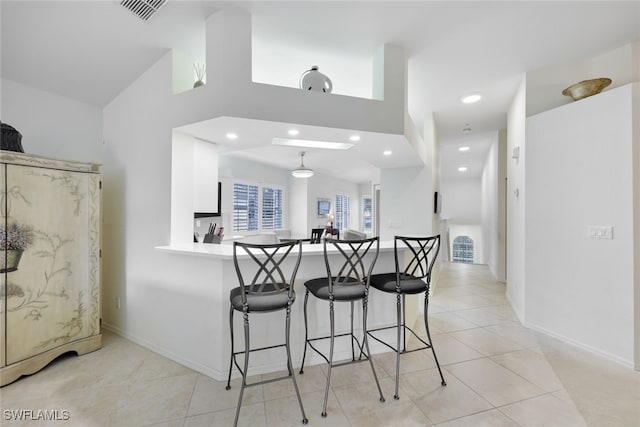 kitchen with a breakfast bar, light tile patterned floors, recessed lighting, visible vents, and a peninsula