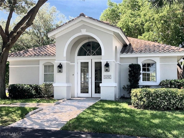 view of exterior entry featuring a tile roof, a lawn, and stucco siding