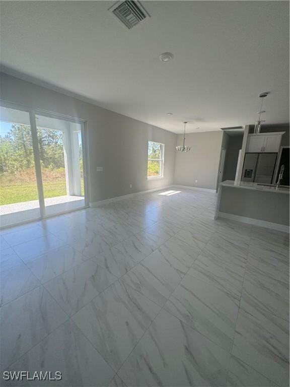 unfurnished living room featuring a notable chandelier, visible vents, marble finish floor, and baseboards