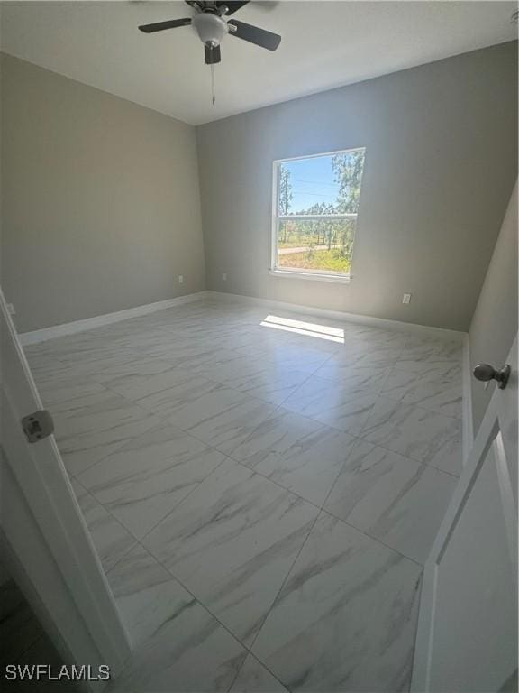 spare room featuring marble finish floor, baseboards, and a ceiling fan