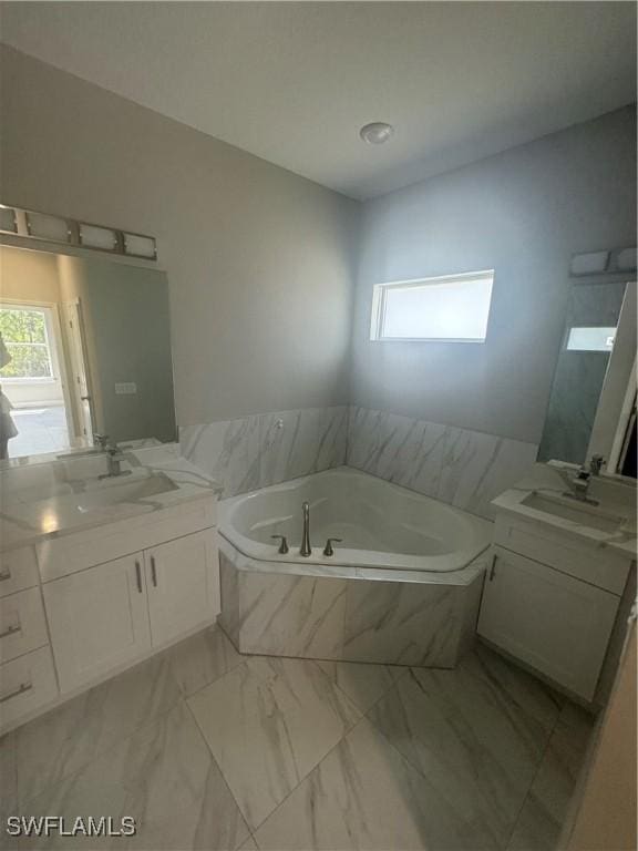 bathroom featuring two vanities, a bath, marble finish floor, and a sink