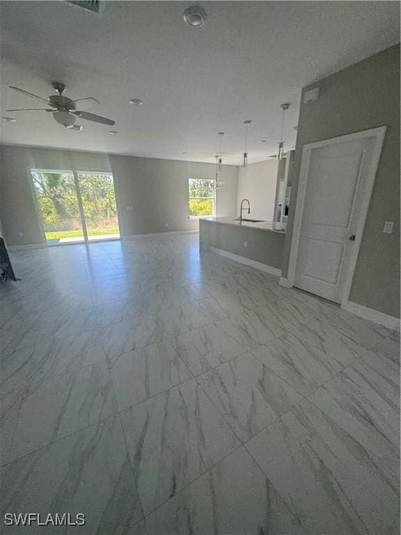 unfurnished living room featuring marble finish floor, ceiling fan, baseboards, and a sink