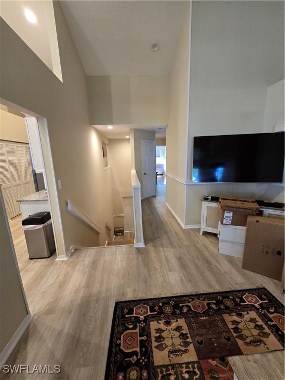 corridor with an upstairs landing, light wood-style flooring, a towering ceiling, and baseboards