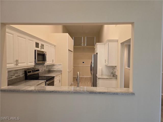 kitchen featuring appliances with stainless steel finishes, tasteful backsplash, white cabinets, a sink, and light stone counters