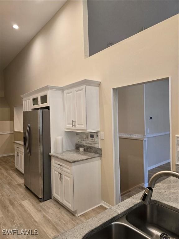 kitchen with stainless steel fridge, light wood-style floors, high vaulted ceiling, white cabinetry, and a sink