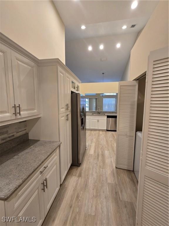 kitchen with black fridge, dishwasher, backsplash, a sink, and light wood-style floors