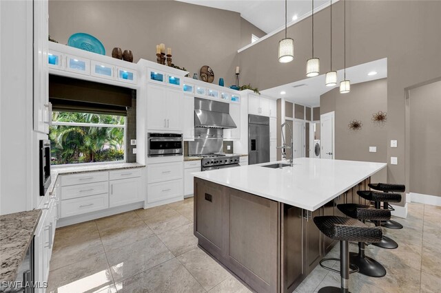 kitchen featuring white cabinetry, an island with sink, wall chimney range hood, and premium appliances