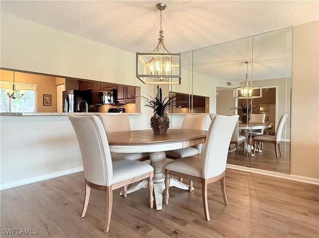 dining room featuring a textured ceiling, a chandelier, and light wood-type flooring