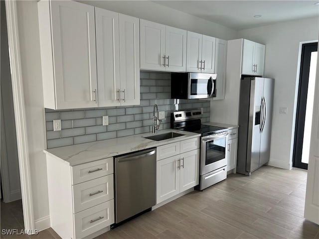 kitchen featuring appliances with stainless steel finishes, sink, white cabinetry, light stone counters, and light hardwood / wood-style floors