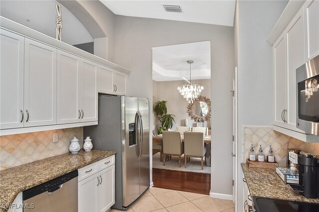 kitchen with stainless steel appliances, white cabinetry, dark stone countertops, and light tile patterned floors