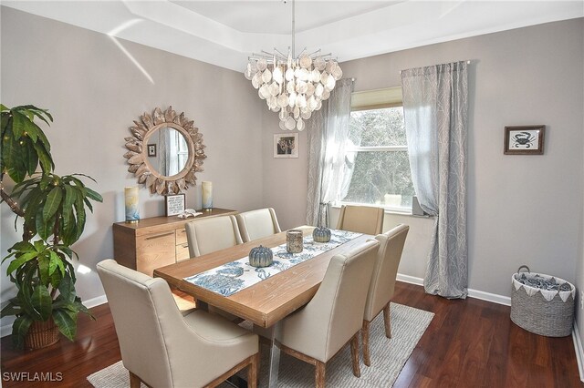 dining area featuring dark wood-type flooring, a tray ceiling, and an inviting chandelier