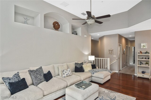 living room featuring dark wood-type flooring, ceiling fan, and a high ceiling