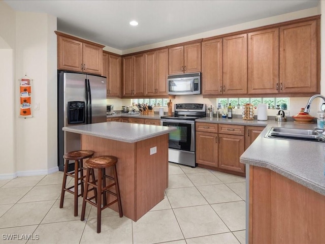 kitchen with sink, light tile patterned floors, a kitchen island, and appliances with stainless steel finishes