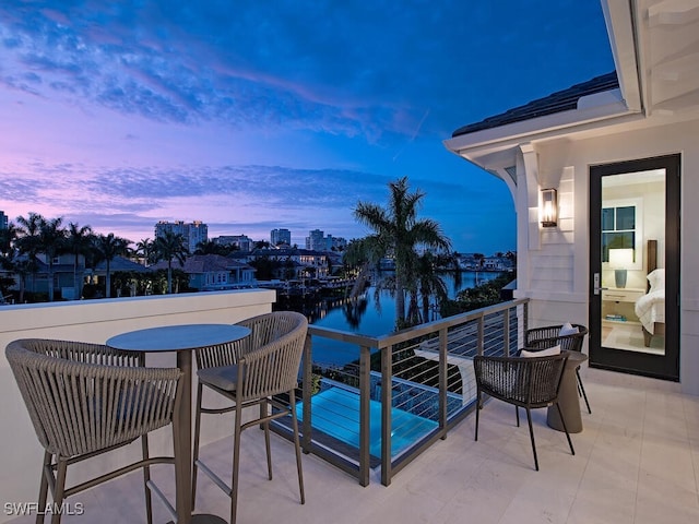 balcony at dusk featuring a water view