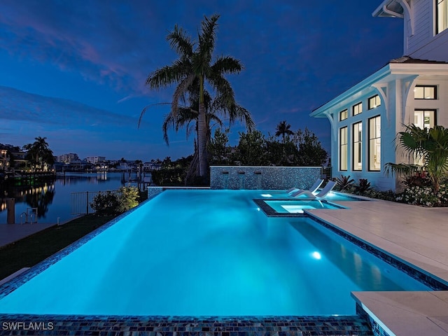 pool at dusk featuring an in ground hot tub, a water view, and a patio area