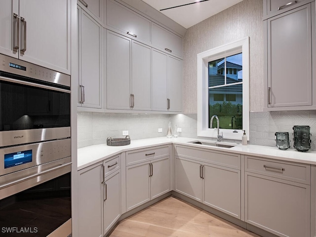 kitchen with double oven, light hardwood / wood-style floors, sink, and backsplash