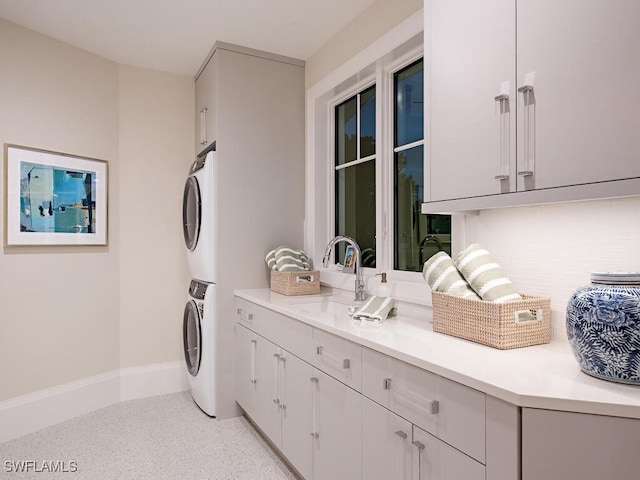 clothes washing area featuring cabinets, stacked washer and clothes dryer, and sink